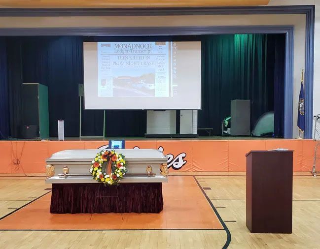 A coffin with a wreath on it is on a stage in a gym.