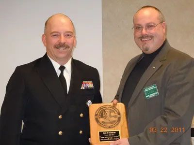 Two men are standing next to each other and one is holding a plaque