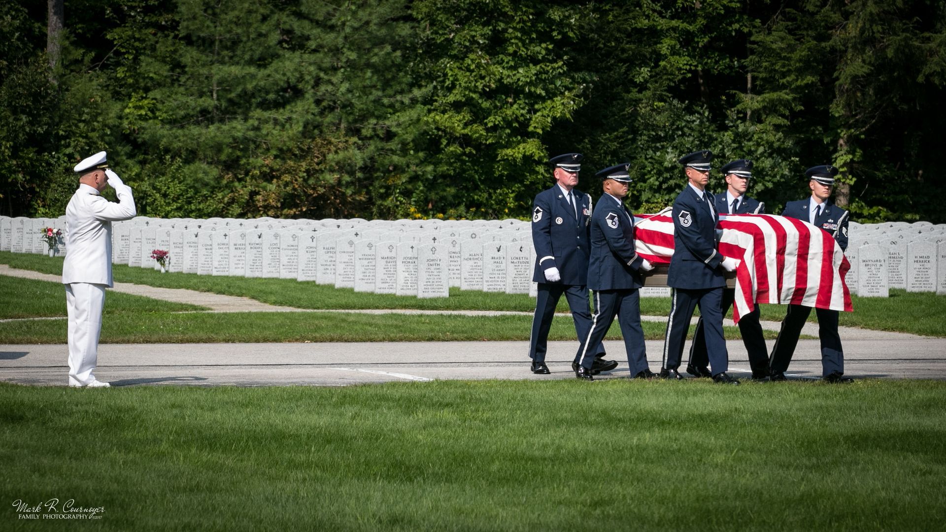 A group of soldiers are carrying an american flag in a cemetery.