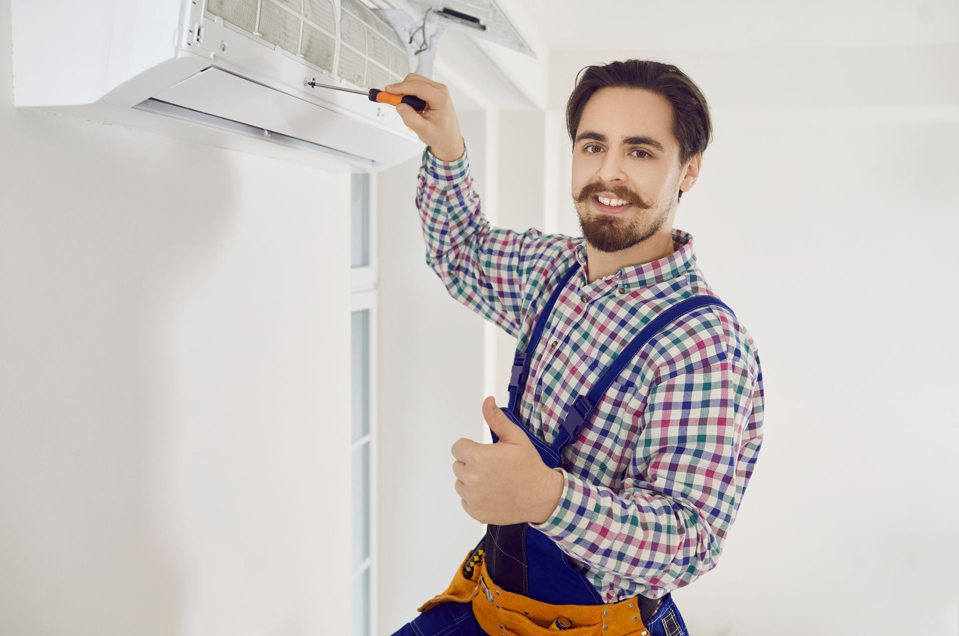 An air conditioning contractor pointing at an air conditioner, holding a screwdriver. An air conditioning contractor pointing at an air conditioner, holding a screwdriver.