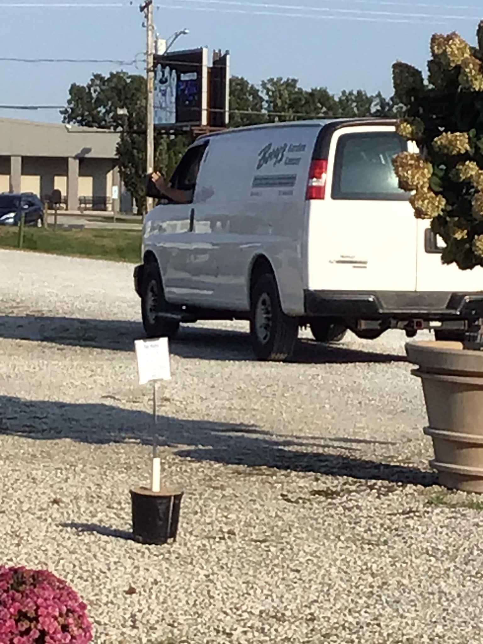 A white van is parked in a gravel lot next to potted plants.
