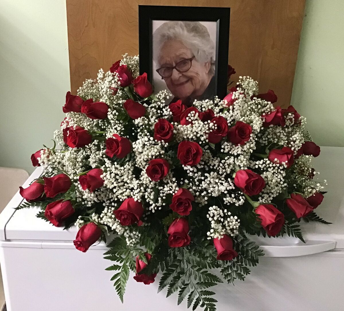 A picture of an elderly woman is surrounded by red roses and baby 's breath