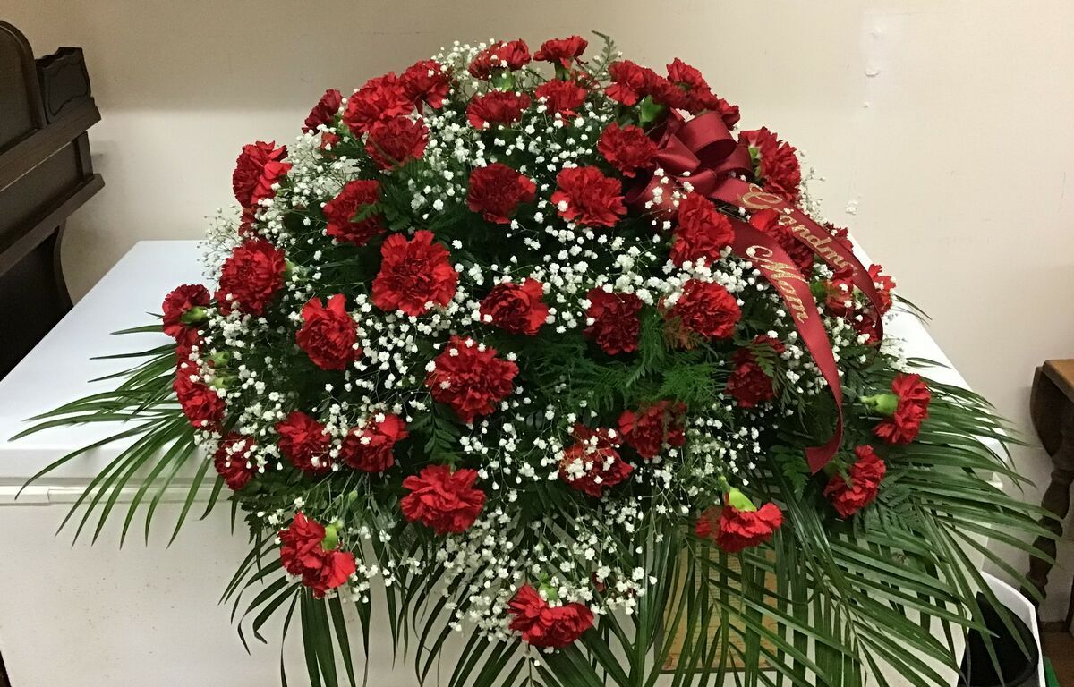 A white coffin covered in red carnations and baby 's breath