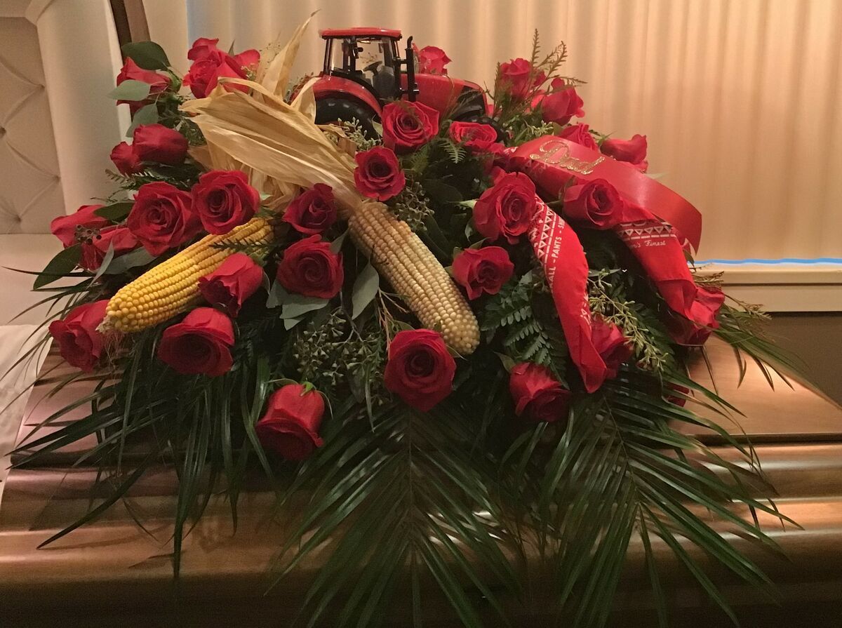 A coffin decorated with red roses , corn and a tractor.