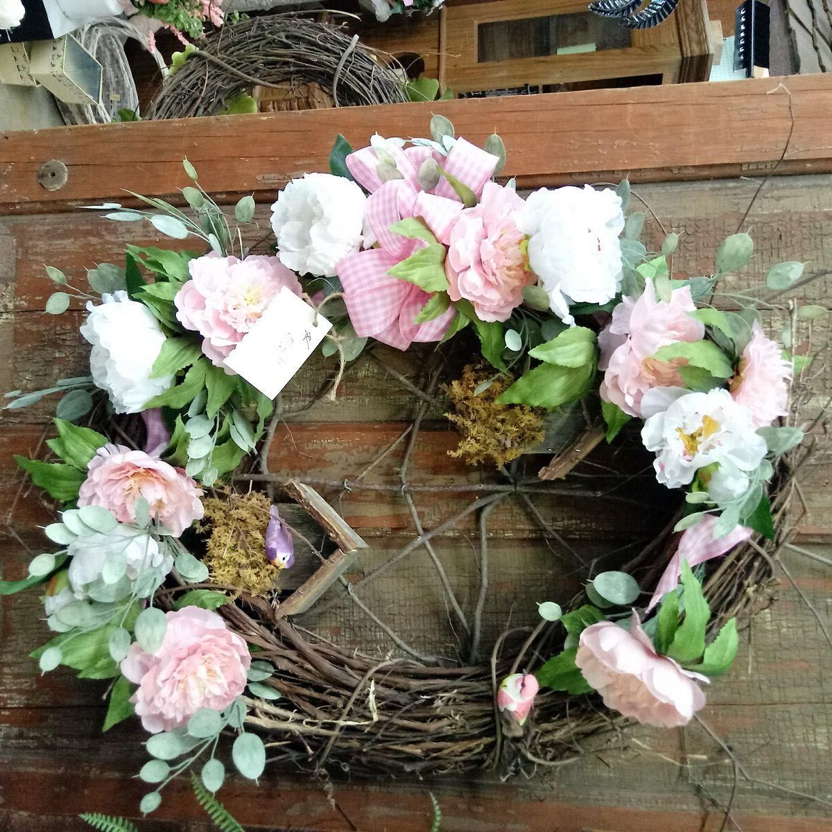 A wreath with pink and white flowers is hanging on a wooden wall.