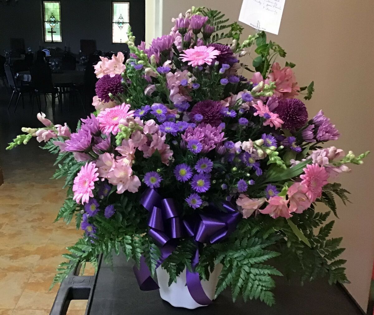 A vase filled with purple and pink flowers with a purple bow.