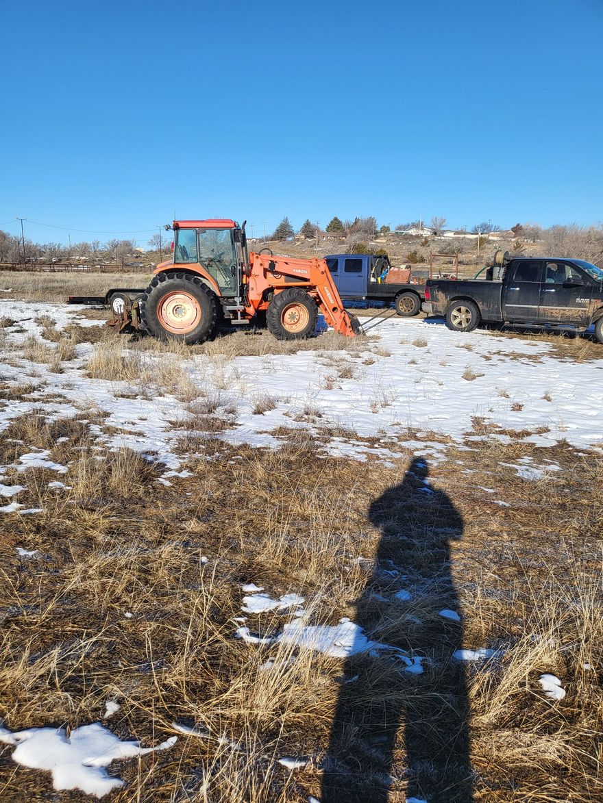 Orange tractor in snowy field, blue truck pulling it, clear sunny day.