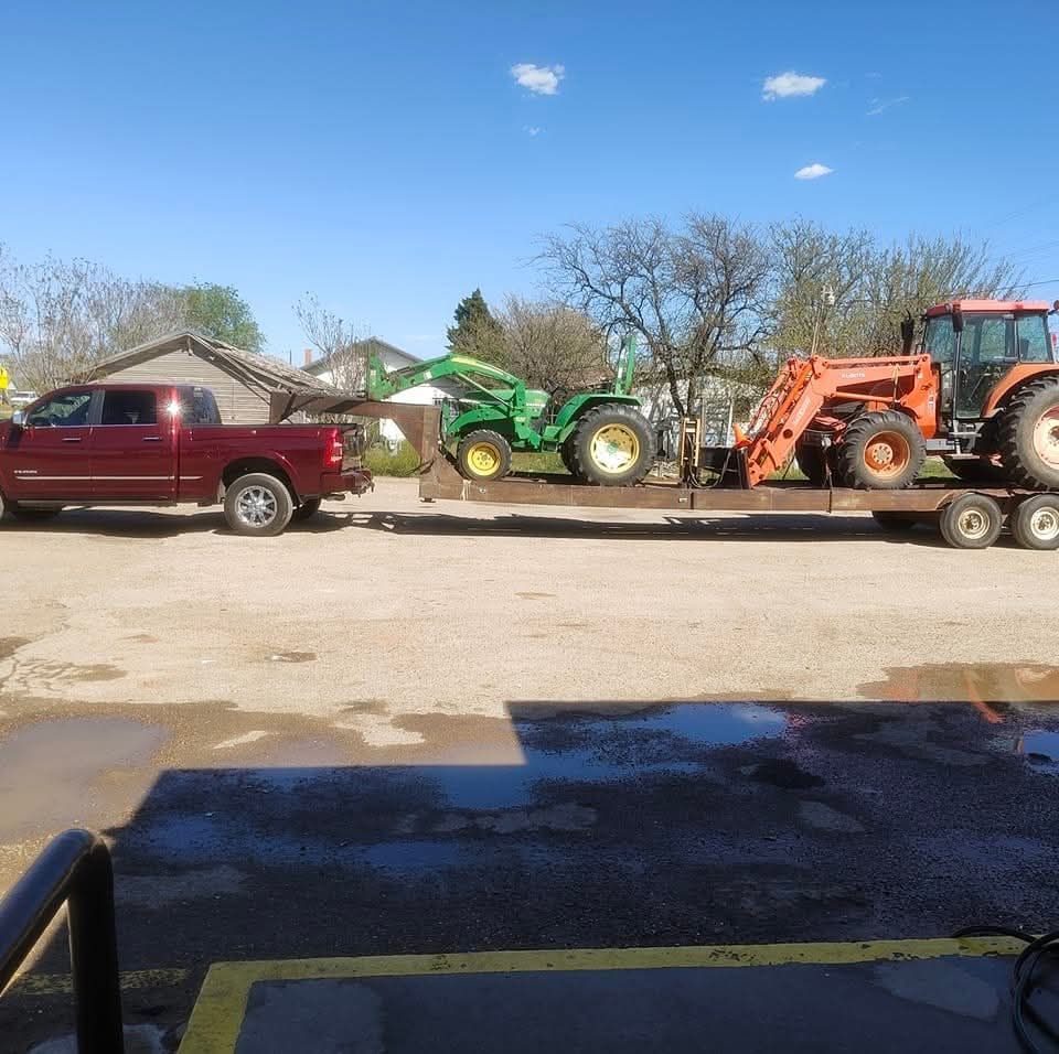 Red truck towing a trailer with two tractors on a sunny day.