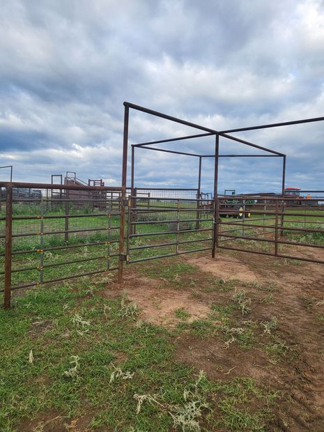 Metal cattle pens on a grassy plain under a cloudy sky.