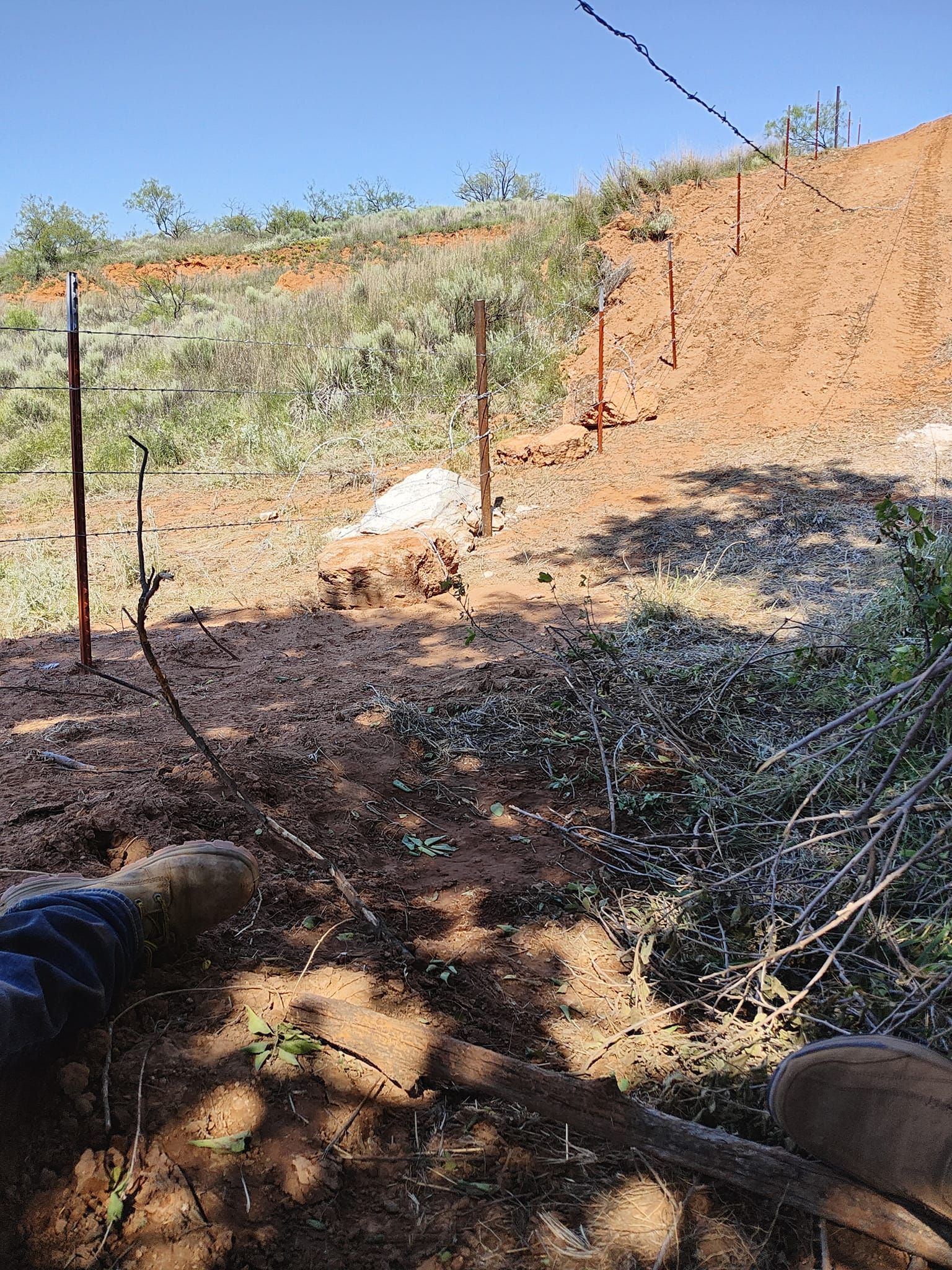 A person's view of a brown hillside with target posts and a few green plants under a bright blue sky.