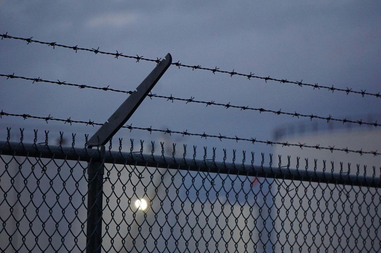 Chain-link fence topped with barbed wire against a dusk sky.