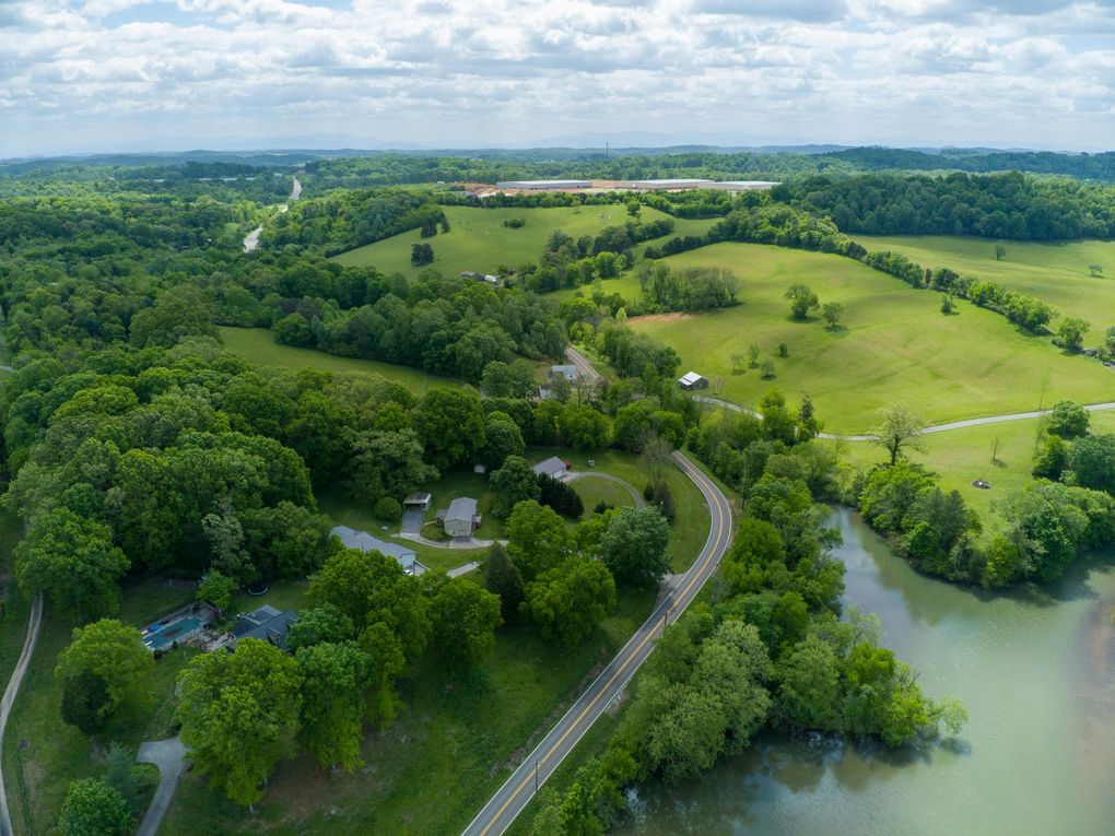Green landscape with trees, fields, road, and water under a cloudy sky.