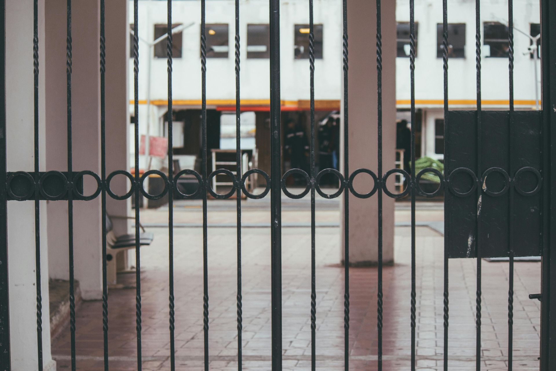 Iron gate with circular accents, leading to a building's entrance. White structure with orange awning in the background.