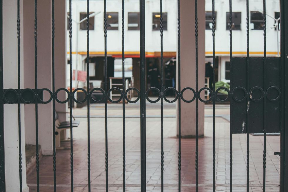 Iron gate with circular accents, leading to a building's entrance. White structure with orange awning in the background.