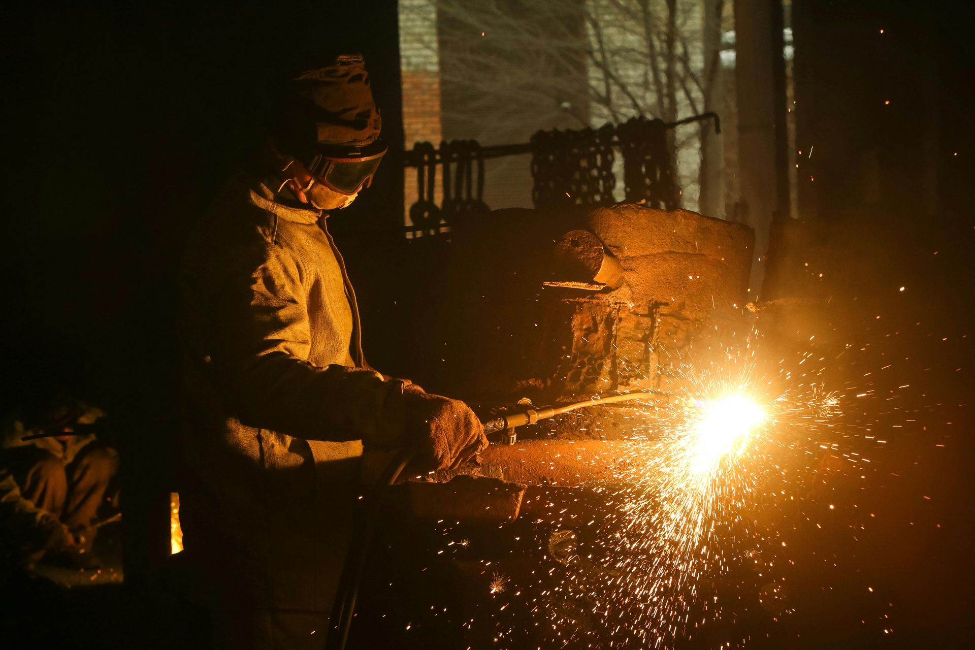 A welder in a dark workshop, sparks flying as they work on metal with protective gear.