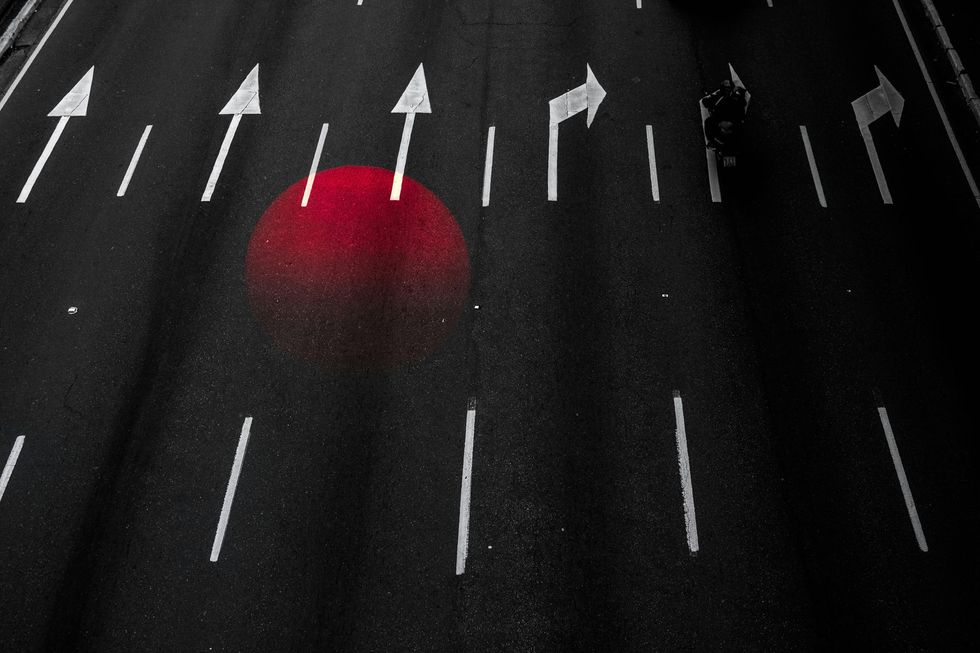 Black asphalt road with white directional arrows and a large, red circle spray painted on the surface.