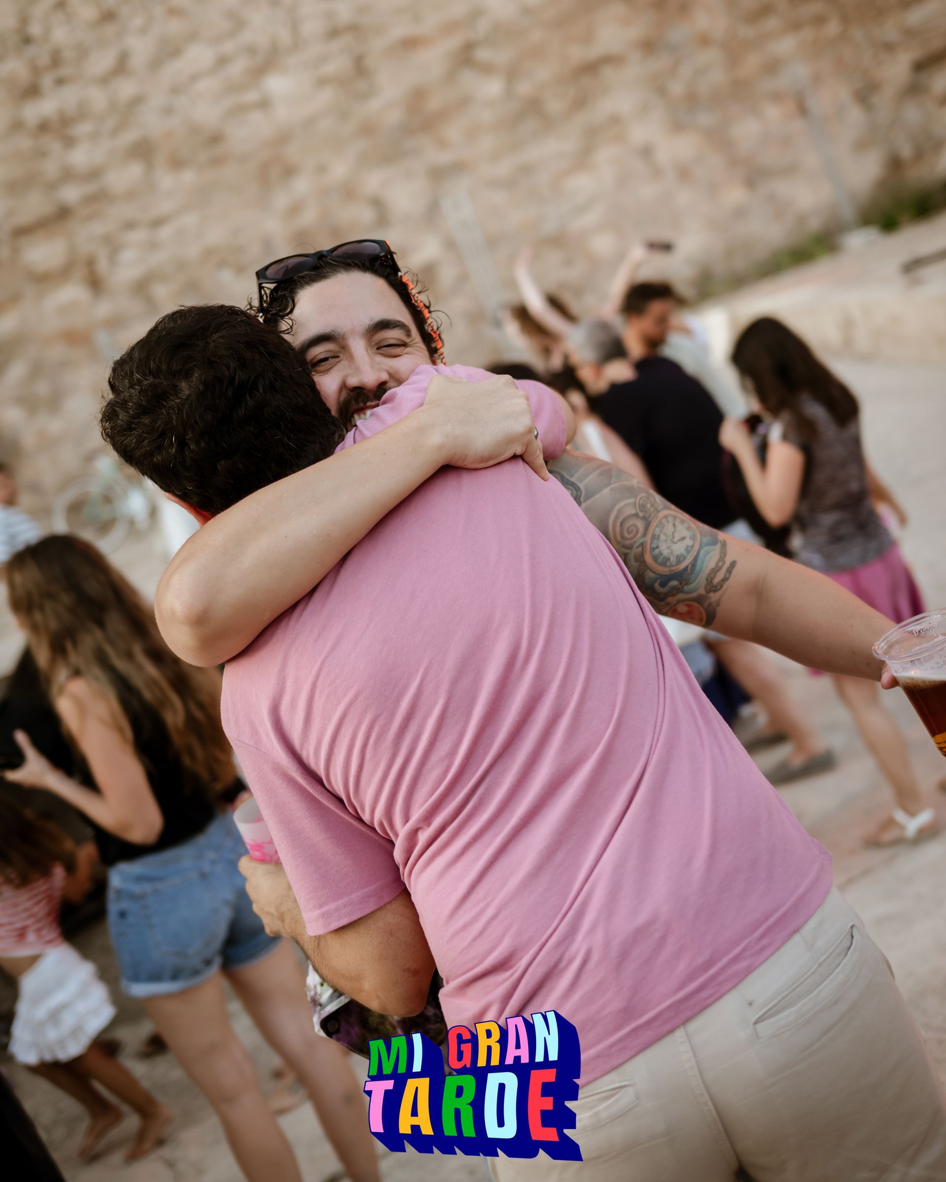 Un hombre con una camisa rosa abraza a otro hombre.