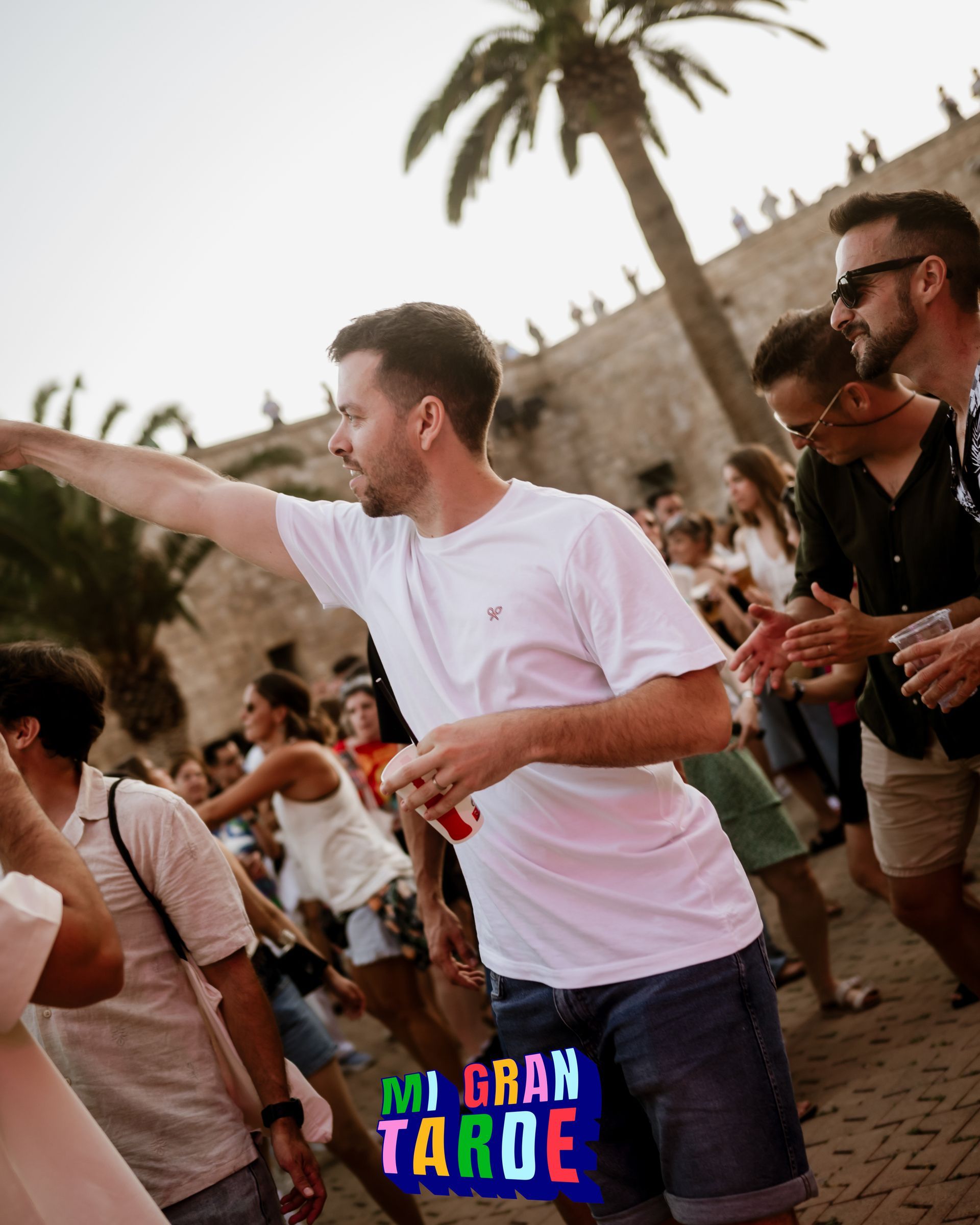 Un hombre con camisa blanca está bailando frente a un cartel que dice mi gran tarde.