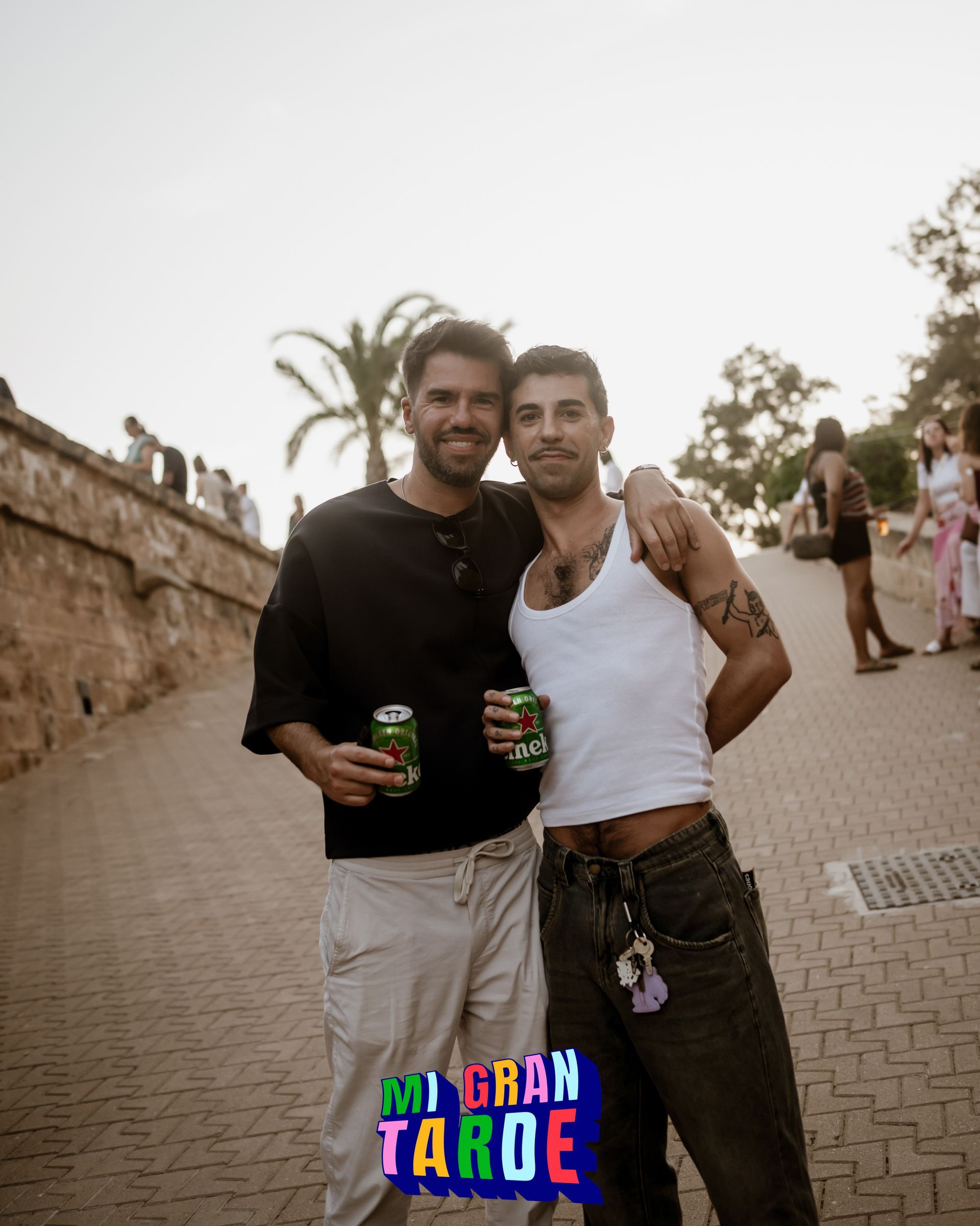 Dos hombres están parados uno al lado del otro en una acera sosteniendo latas de refresco.