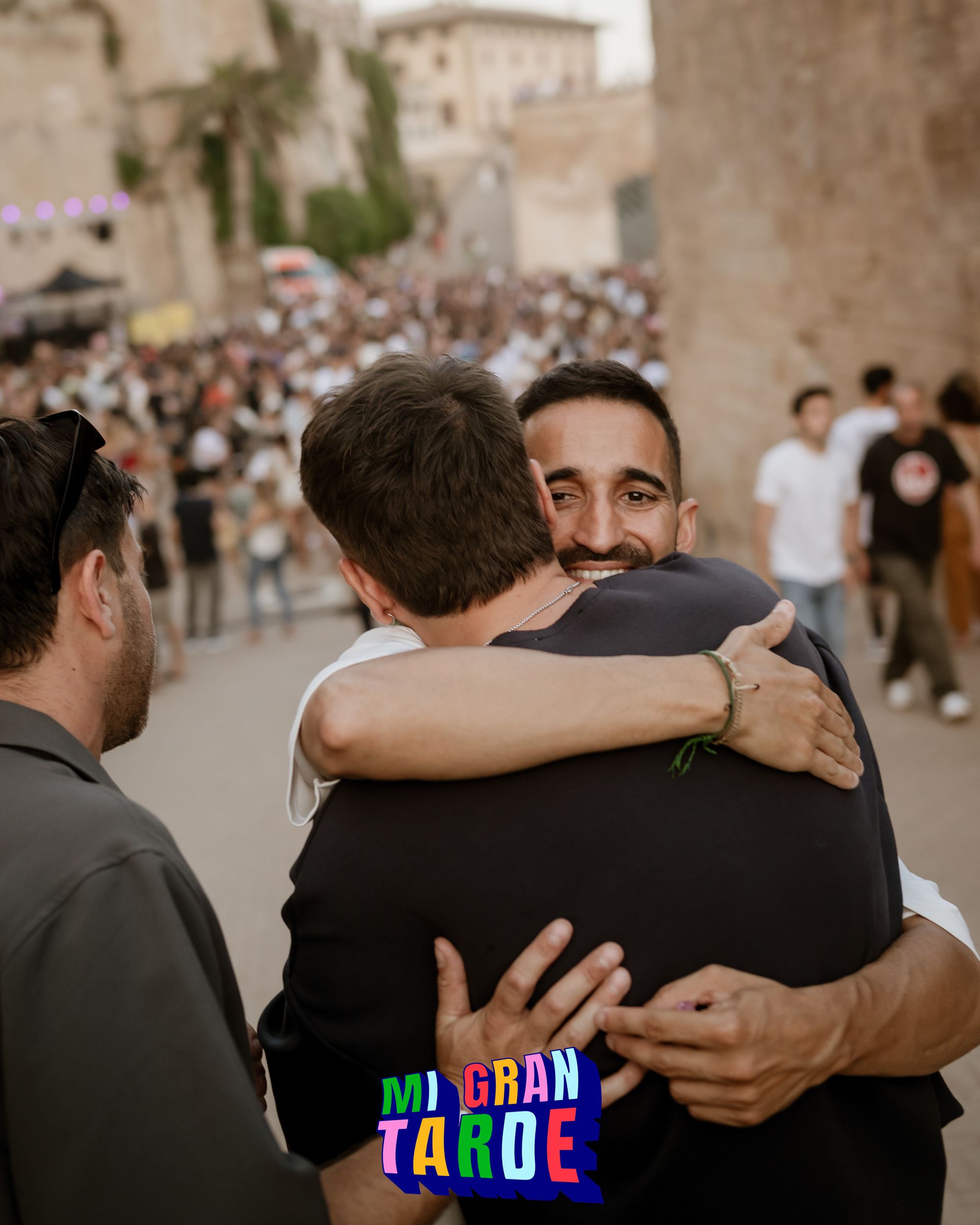 Dos hombres abrazándose frente a una multitud con un cartel que dice mi gran tarde