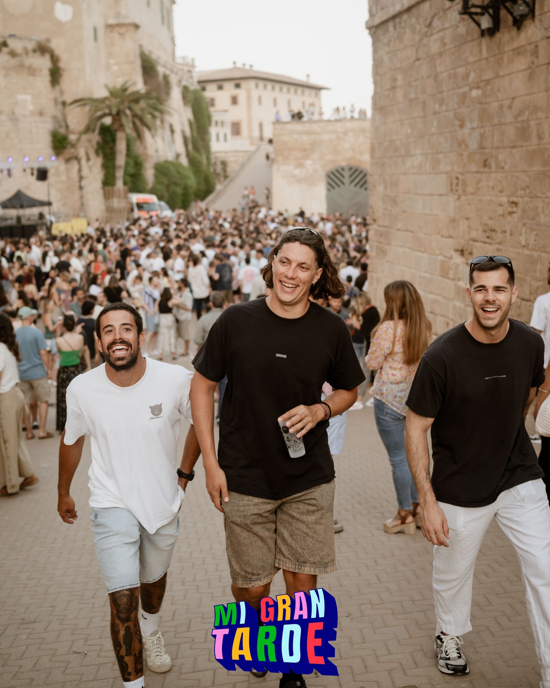 Tres hombres caminan por una calle frente a una multitud de personas.