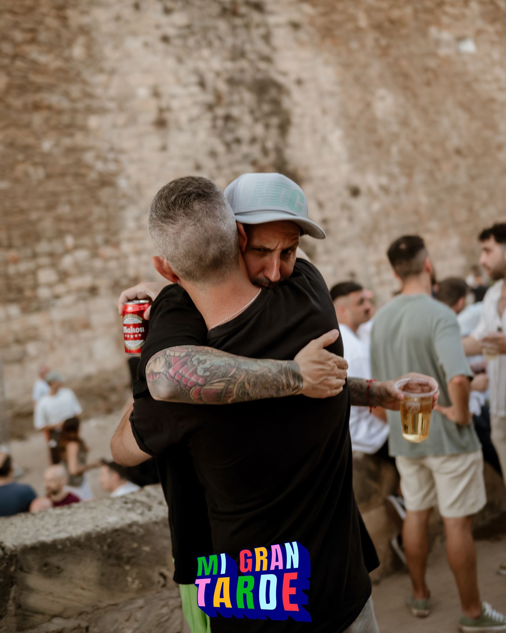 Dos hombres abrazándose frente a un cartel que dice mi gran tarde