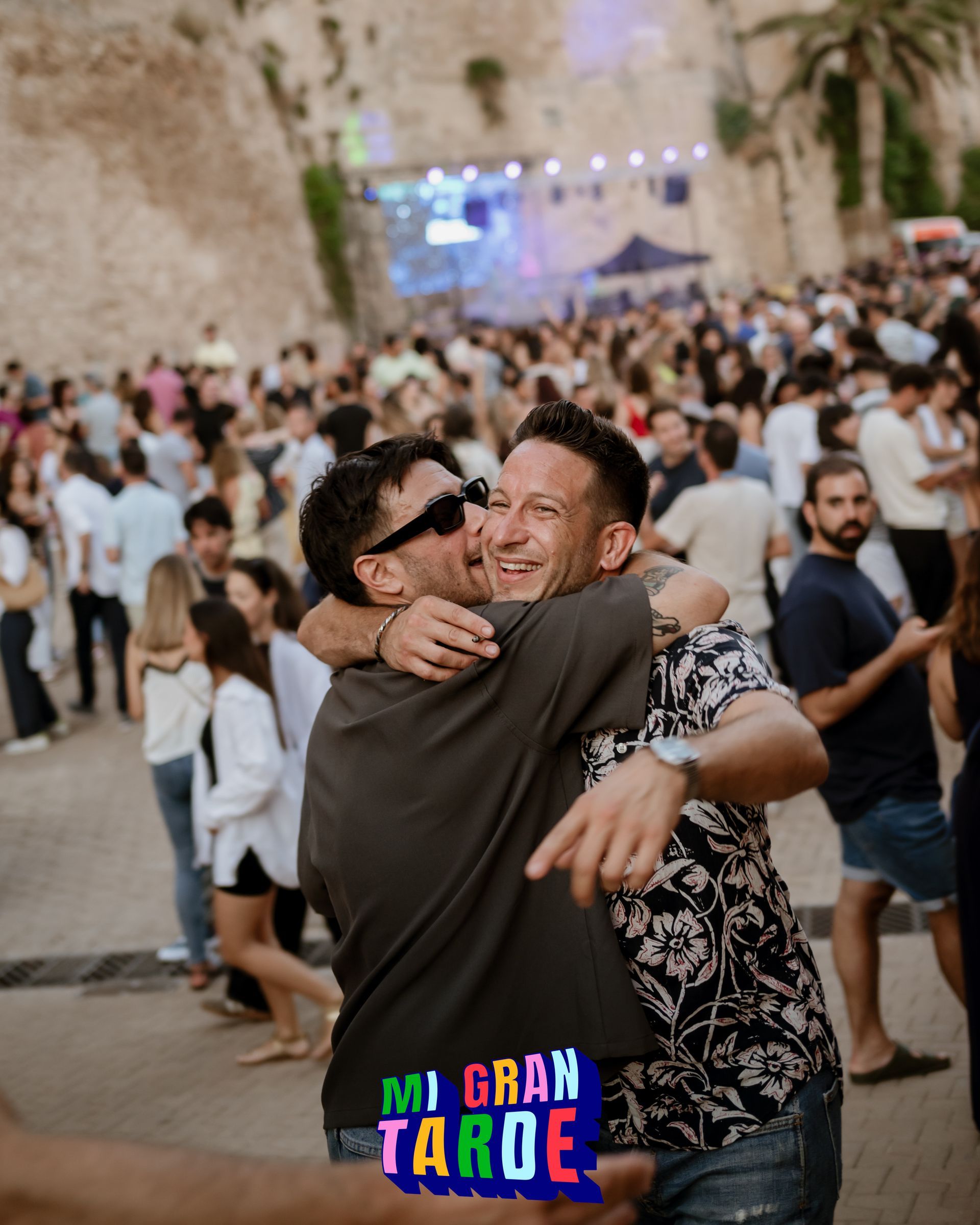 Dos hombres abrazándose frente a una multitud con un cartel que dice mi gran tarde