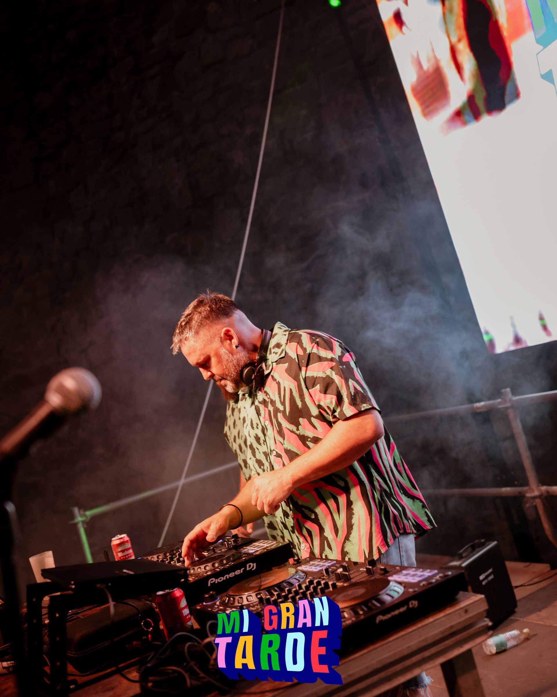 Un hombre está tocando un set de DJ frente a una pantalla grande.