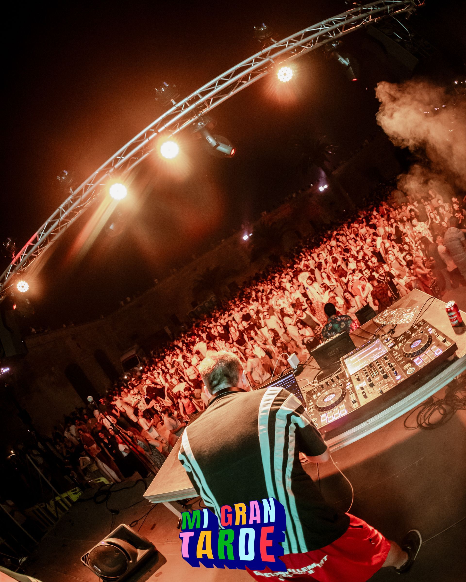 Un DJ está tocando música frente a una multitud con un cartel que dice gran tarde