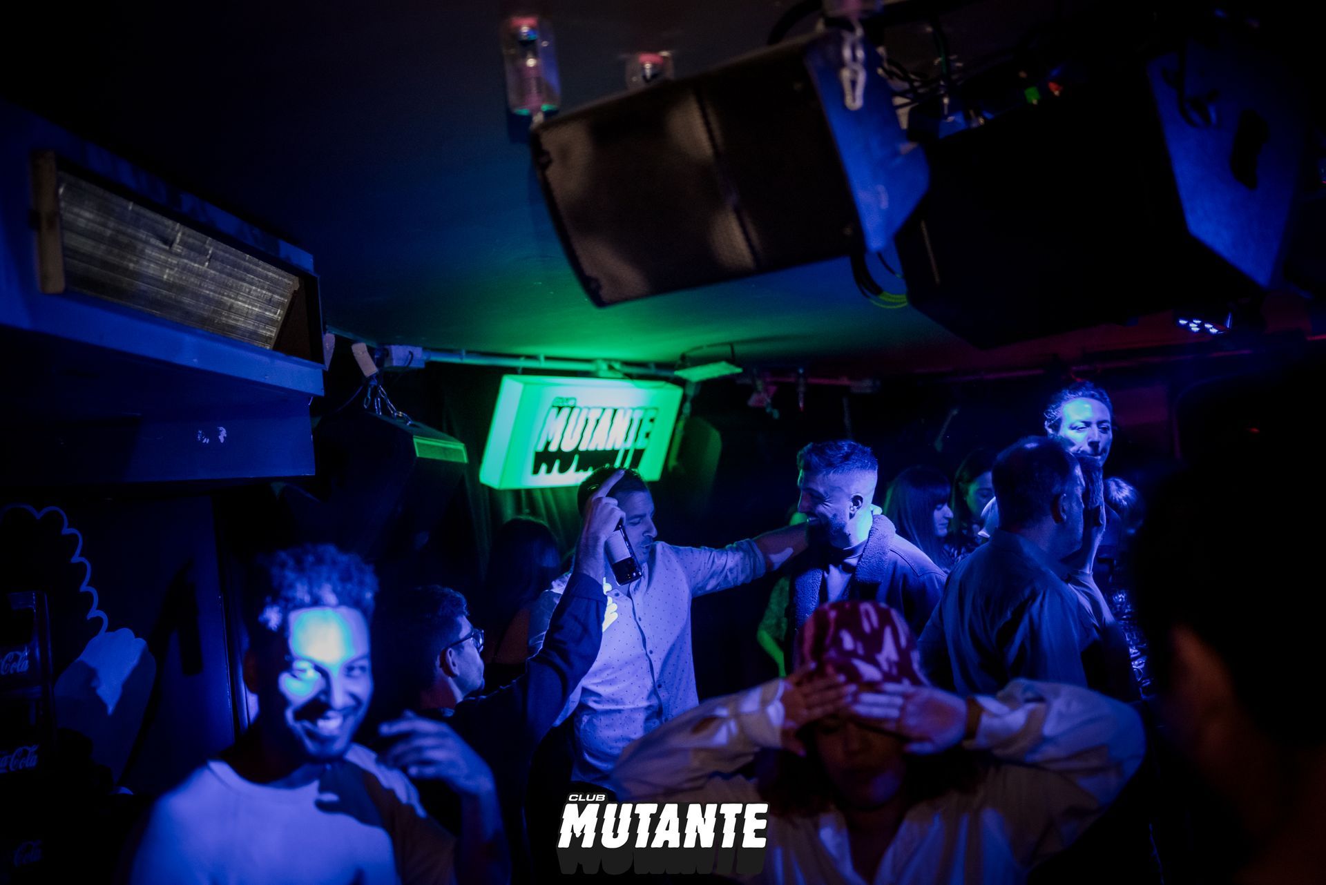 Un grupo de personas está bailando en una habitación oscura con un cartel que dice mutante.