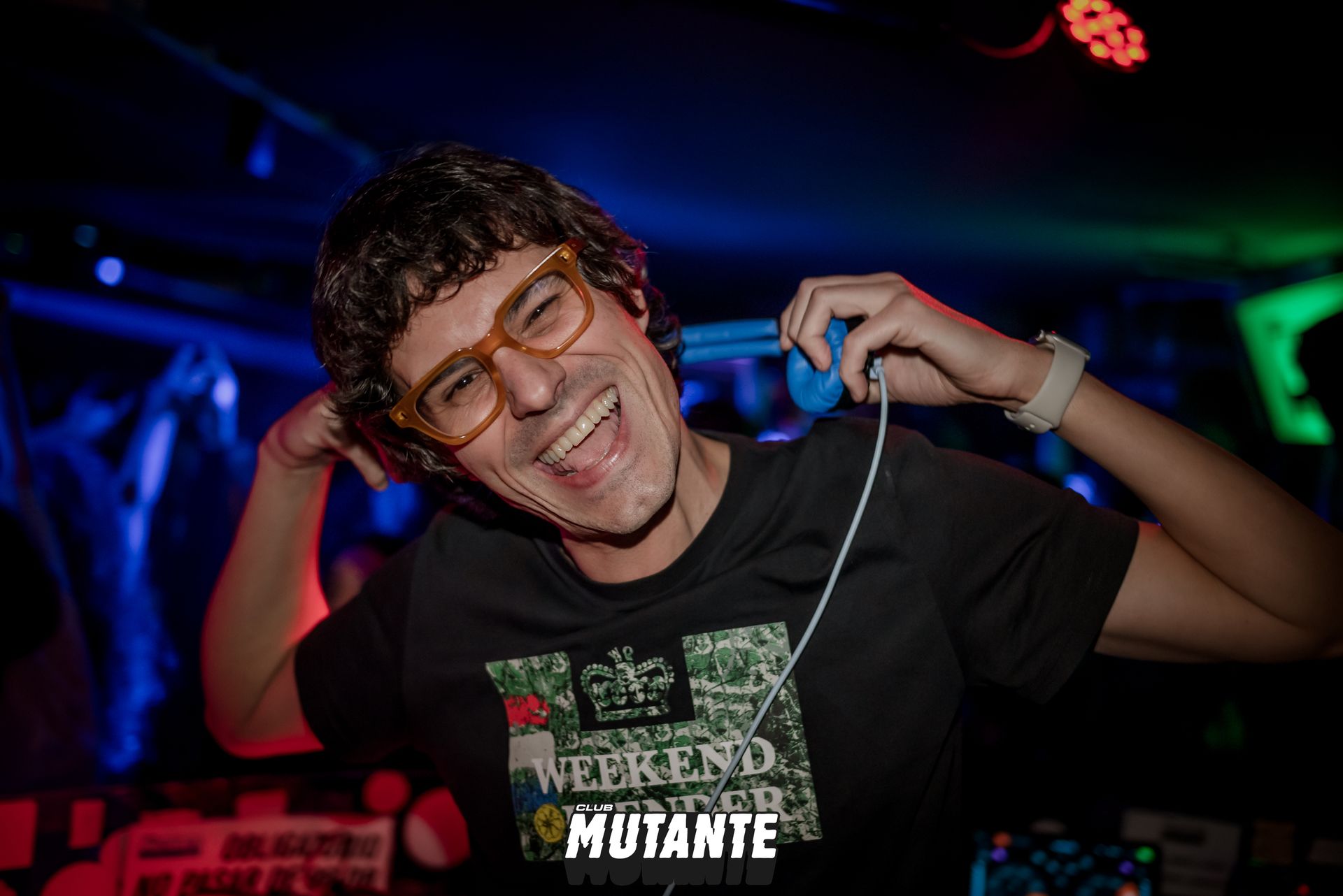 Un hombre que lleva gafas y auriculares sonríe en una habitación oscura.