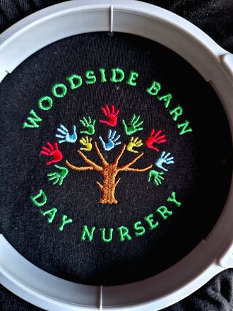 A woodside barn day nursery logo is embroidered on a black shirt