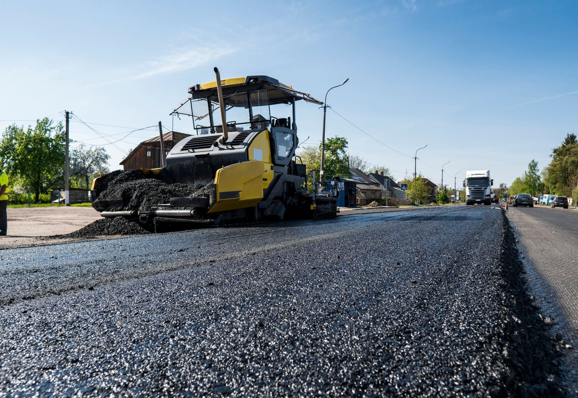 A bulldozer is laying asphalt on the side of a road.