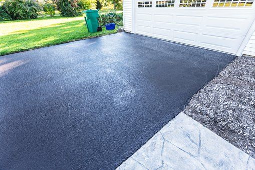 A black asphalt driveway next to a white garage door.