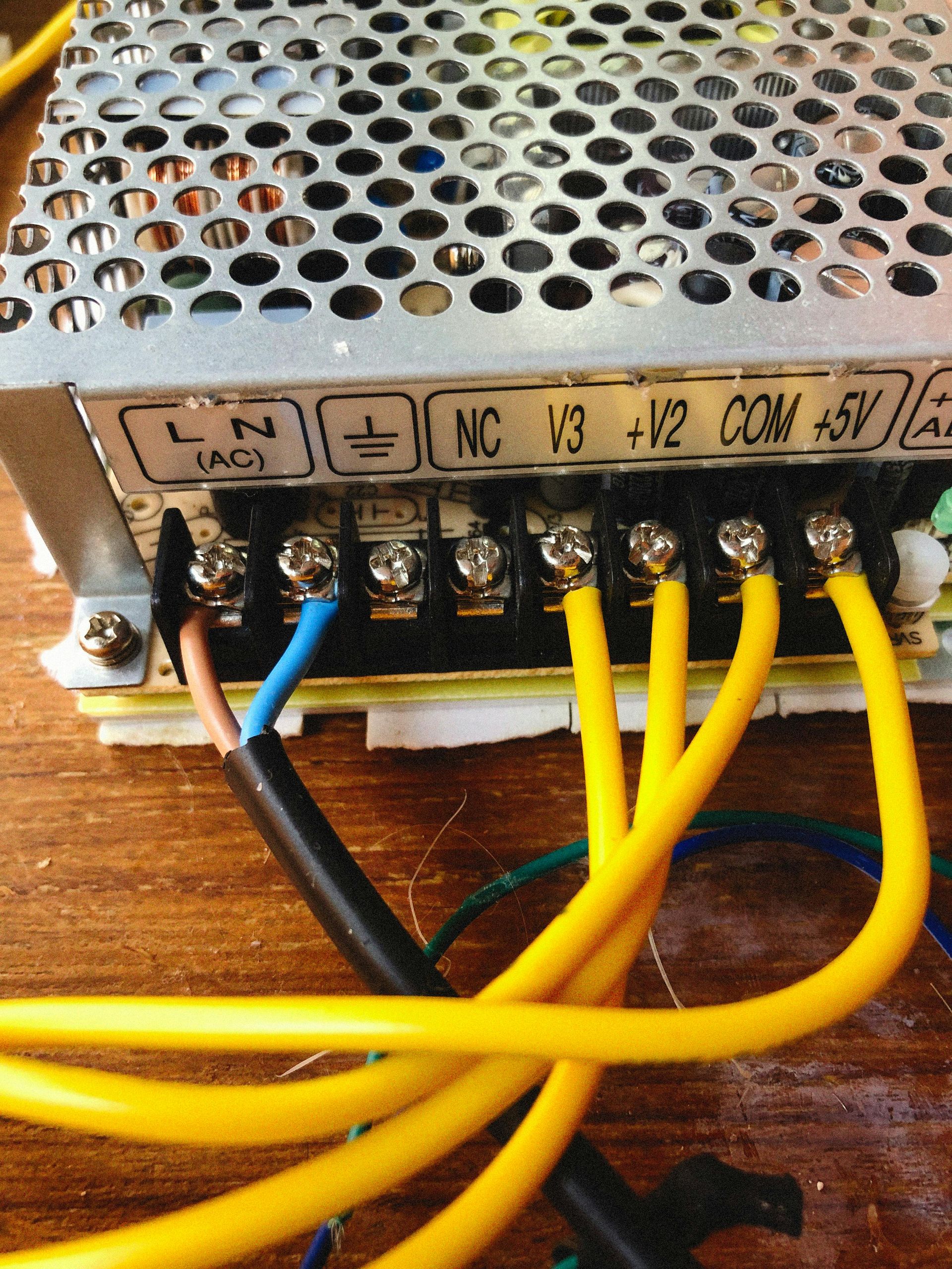 Power supply unit with wires attached to terminals. The wires are yellow, brown, and blue.