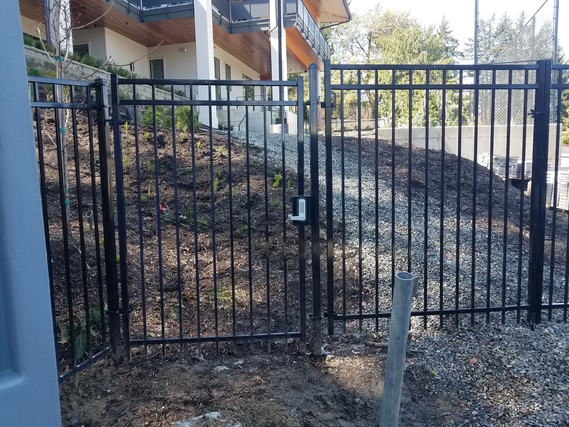 Black metal fence and gate on a slope, leading to a building.