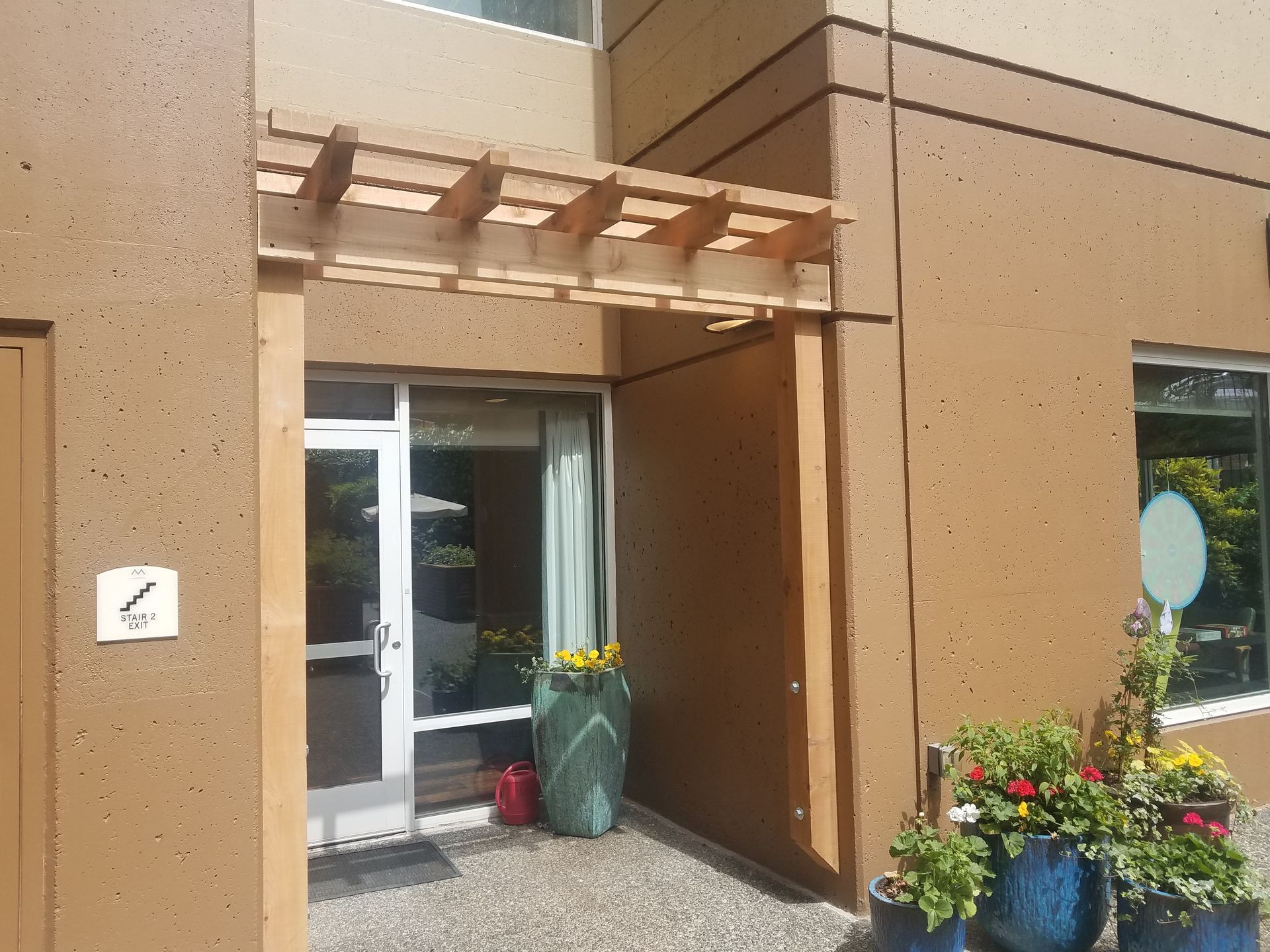 Exterior entrance with a wooden pergola, glass door, and potted flowers.