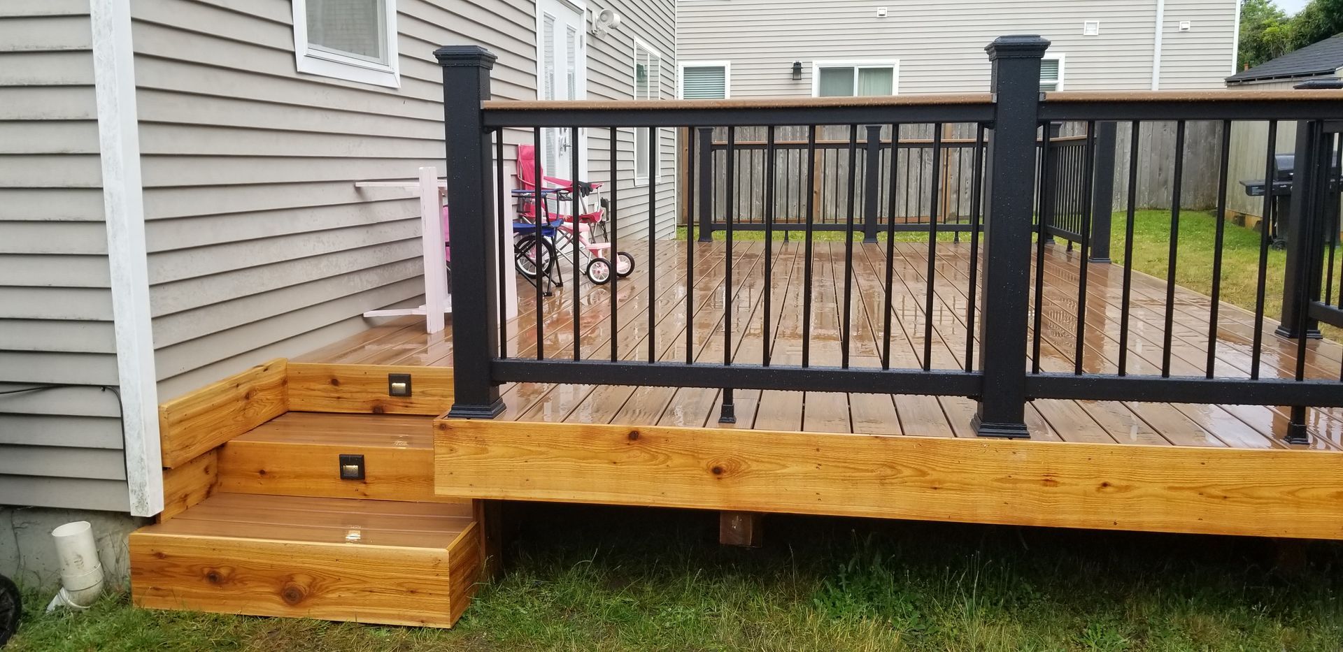 A wooden deck with black railings and steps leading down to a green lawn.