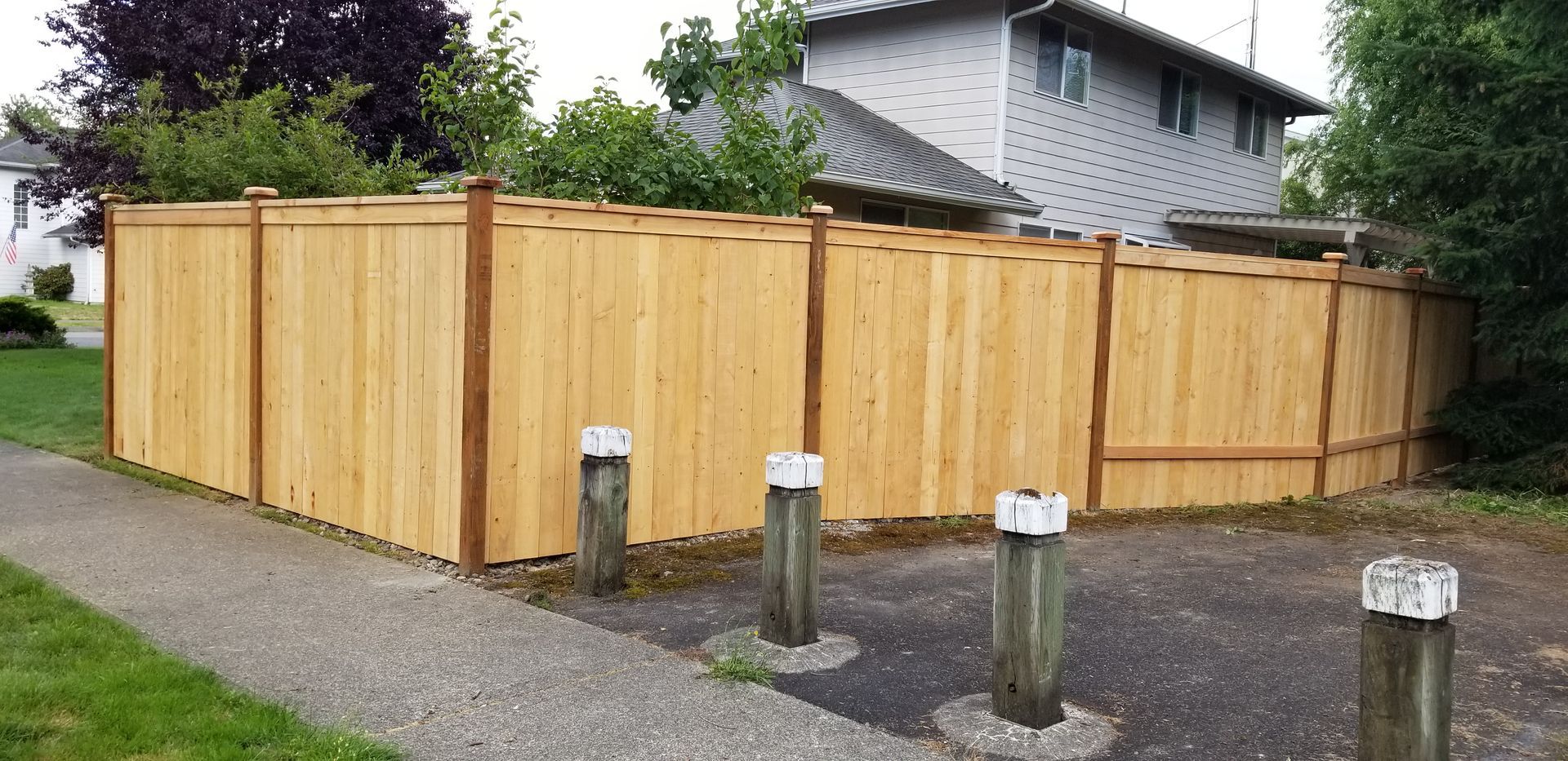 Wooden fence in front of a house, set on gravel, with bollards along the front.