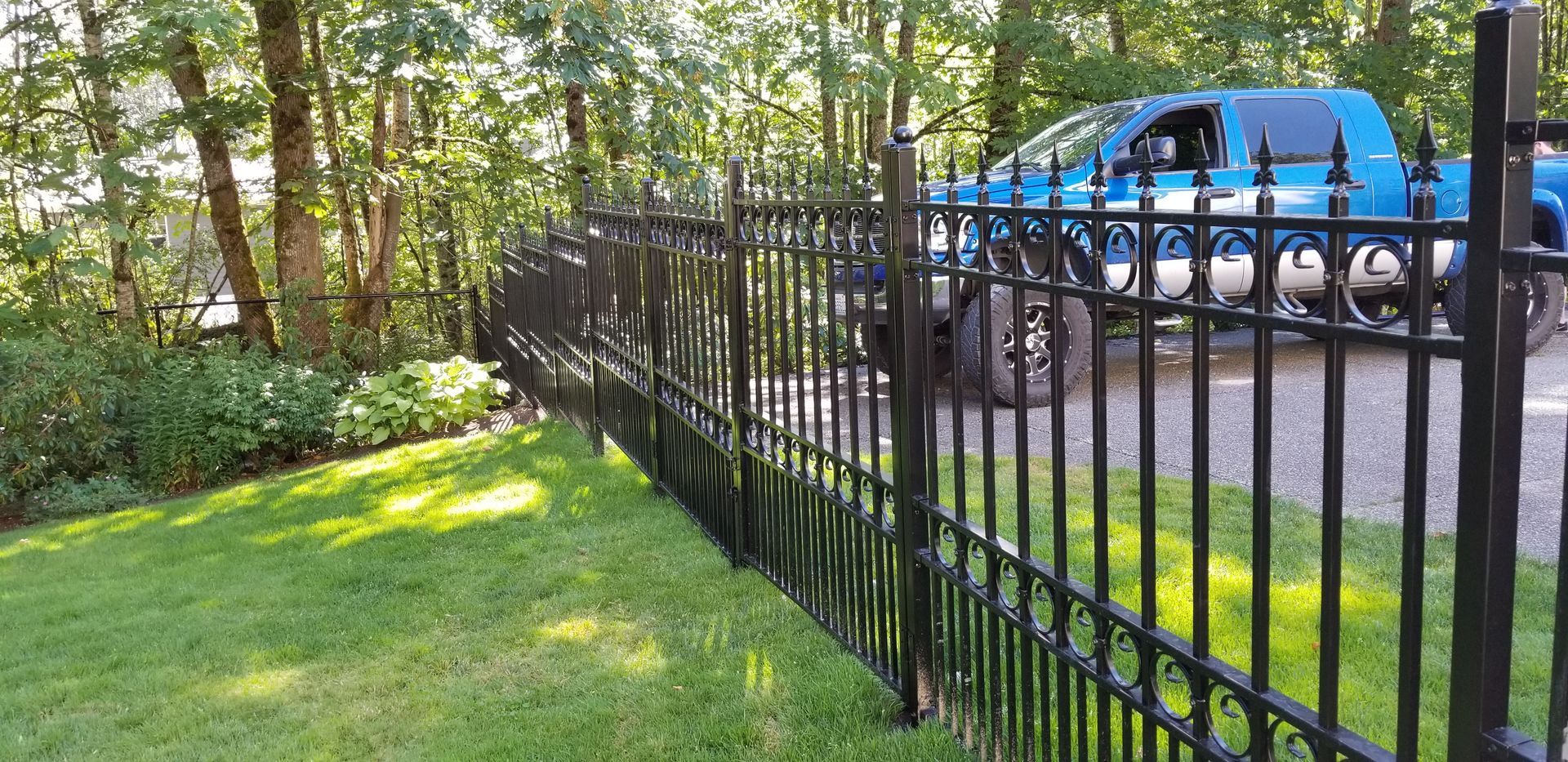 Black metal fence bordering a green lawn with a blue truck parked in the driveway behind it.