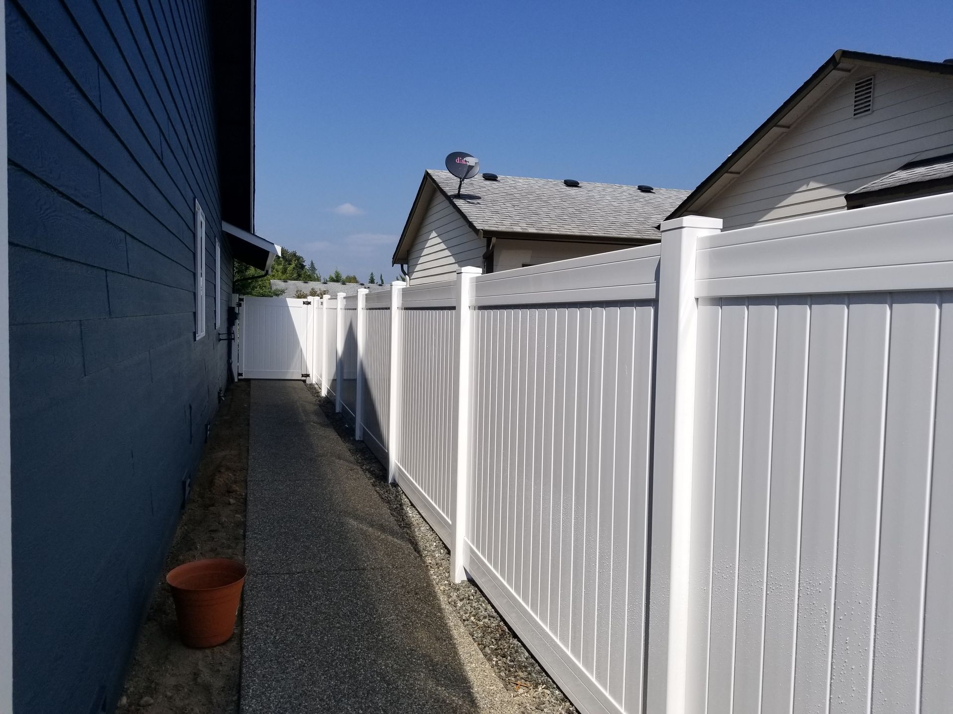 White vinyl fence next to a house with a blue exterior and gravel pathway.