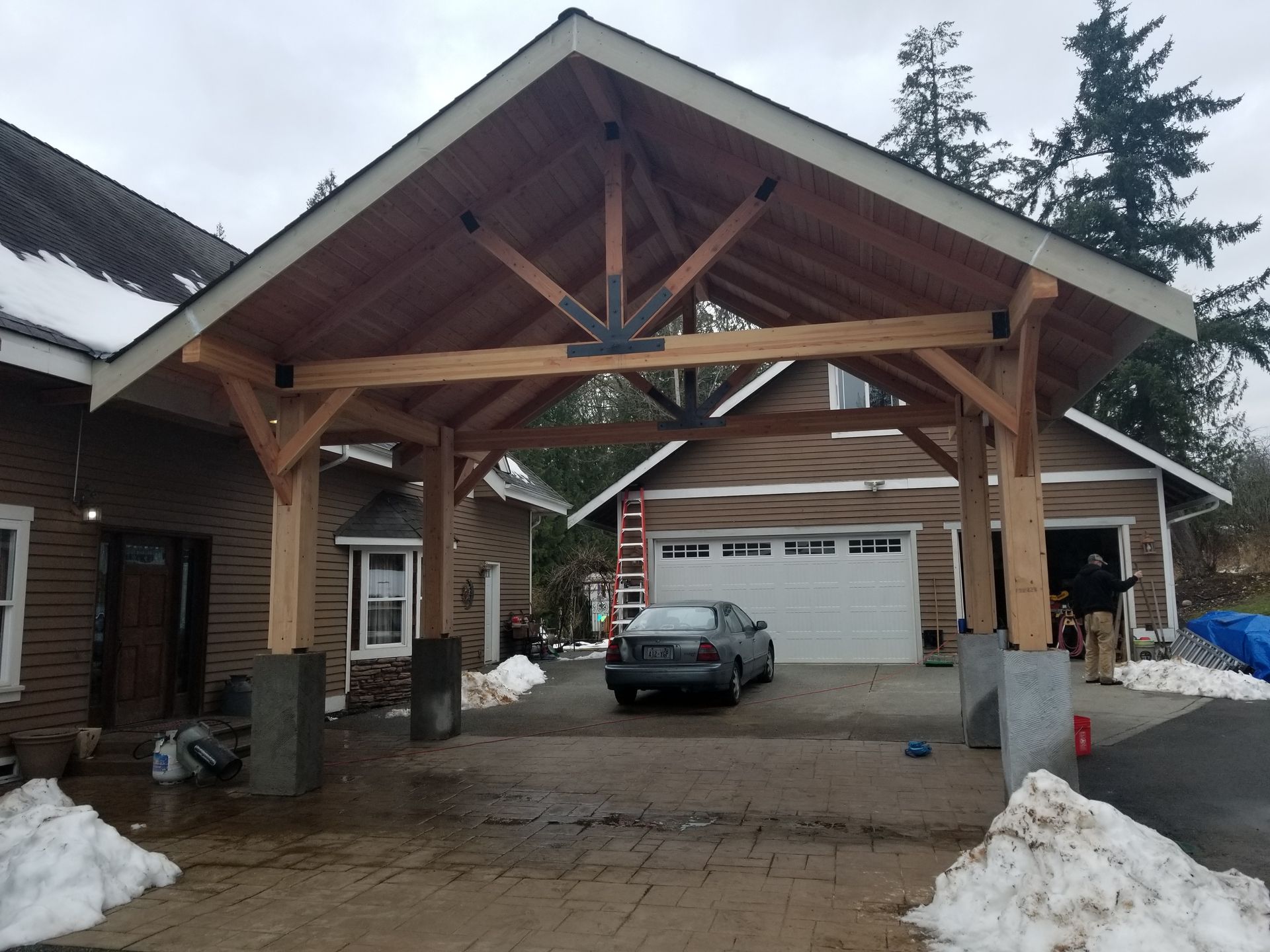 Carport with wooden beams and a car parked inside. Snow on the ground.