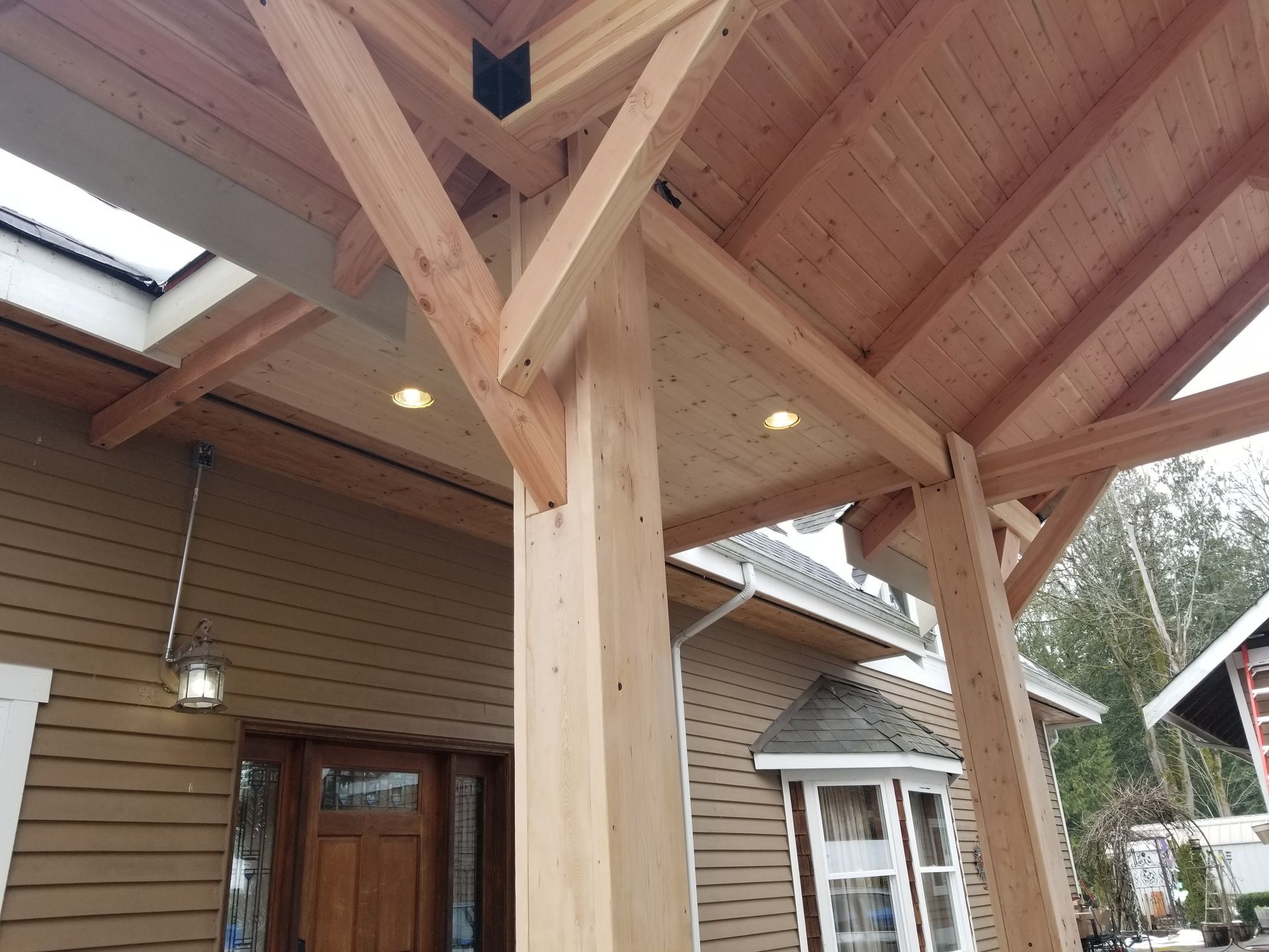 Wooden porch roof supported by columns, with a light brown house in the background.