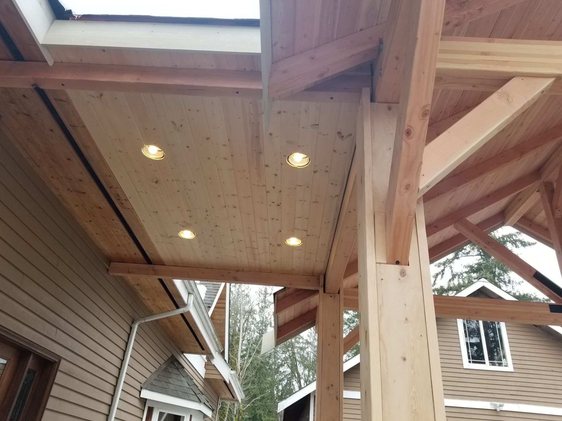 Wooden porch ceiling with recessed lights, supported by beams and columns.