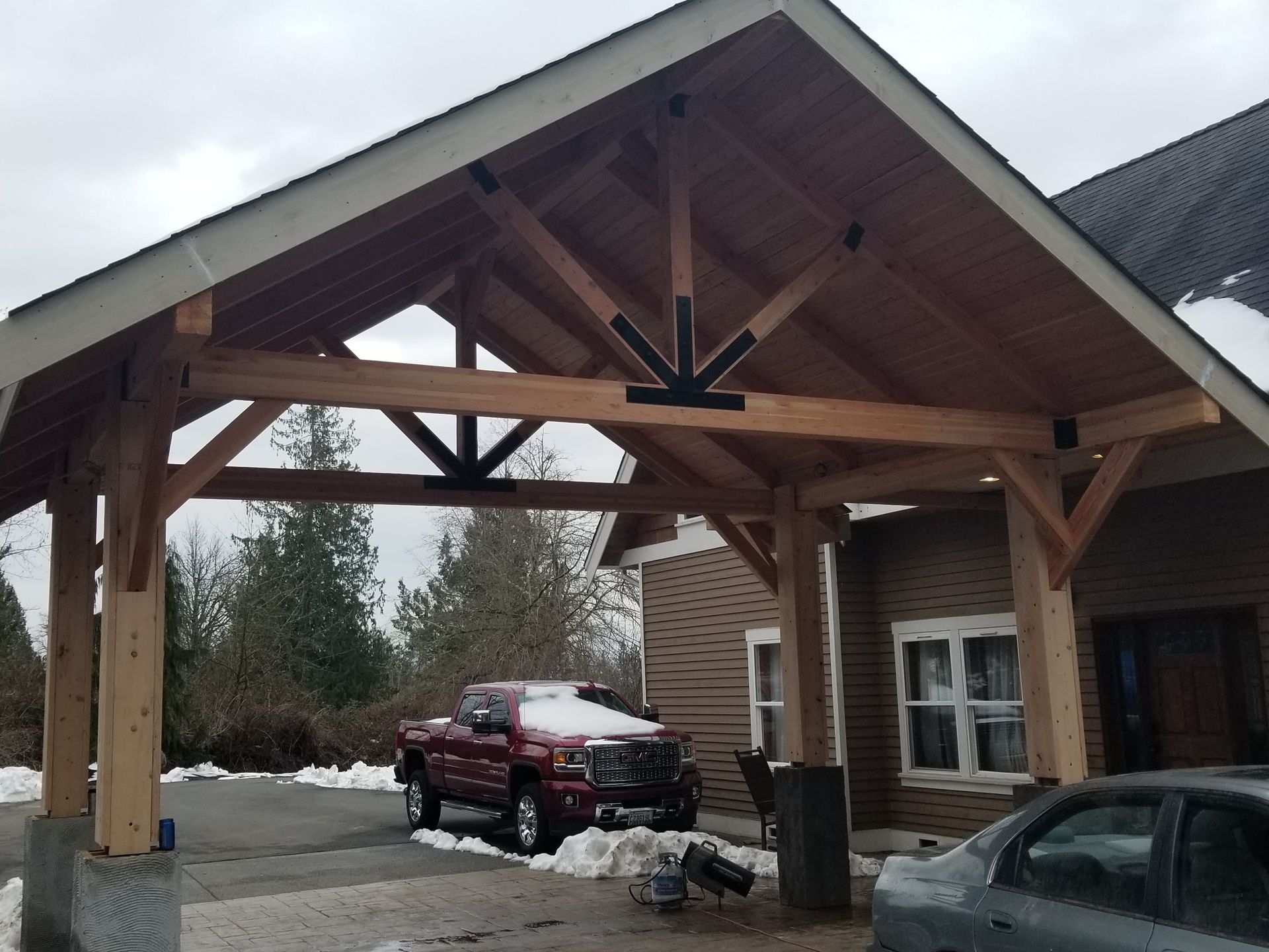 Carport with wooden frame, red truck, snow, brick building.
