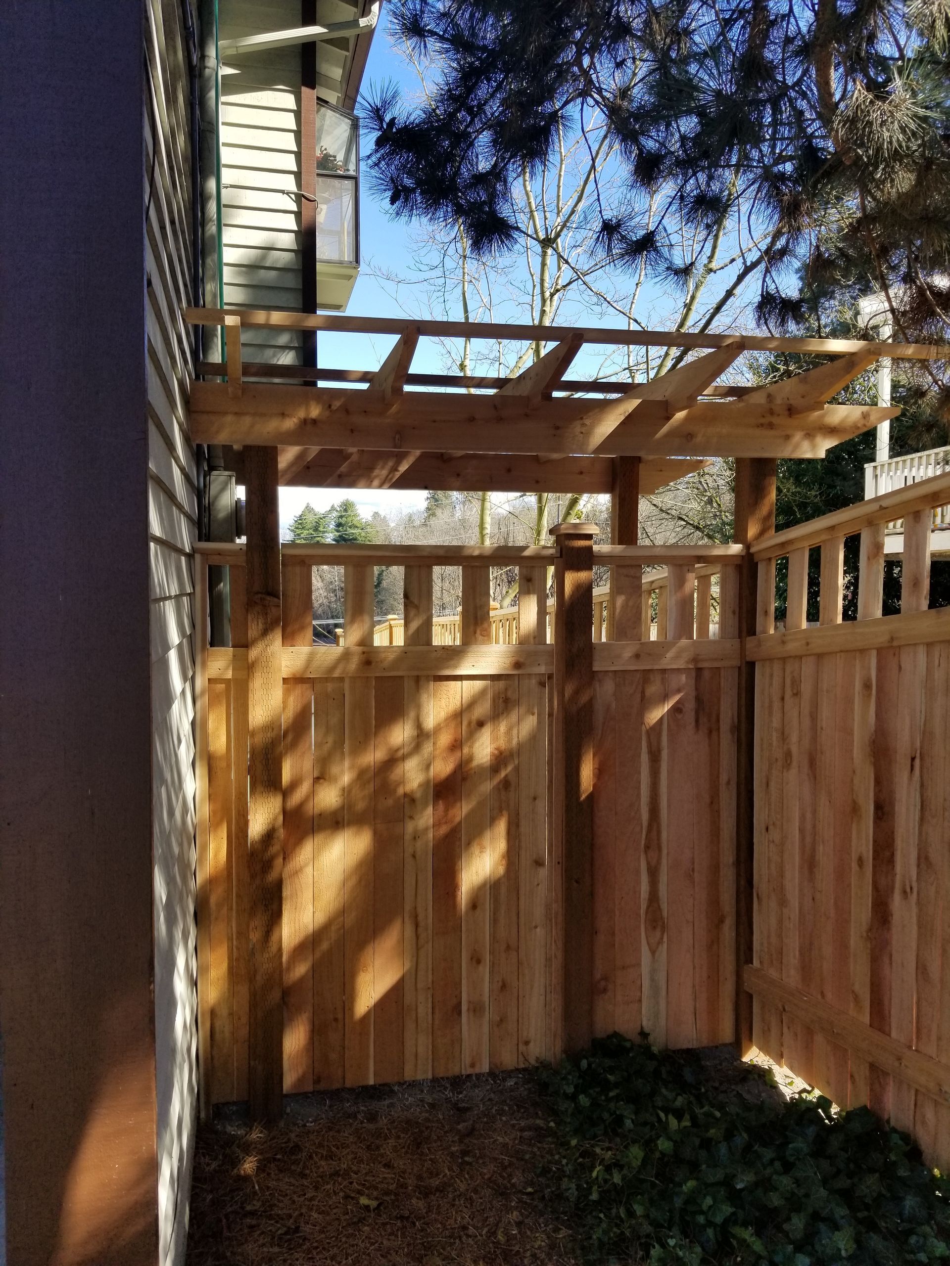 Wooden fence with pergola overhead against a house.