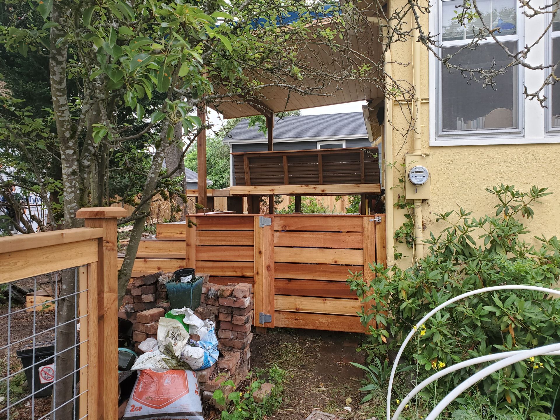 Wooden fence and gate leading to a raised wooden deck attached to a yellow building.