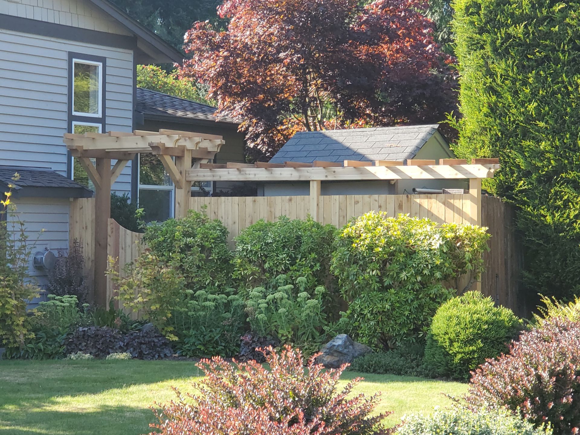 Wooden fence with arbor, front yard, bushes, house in background.