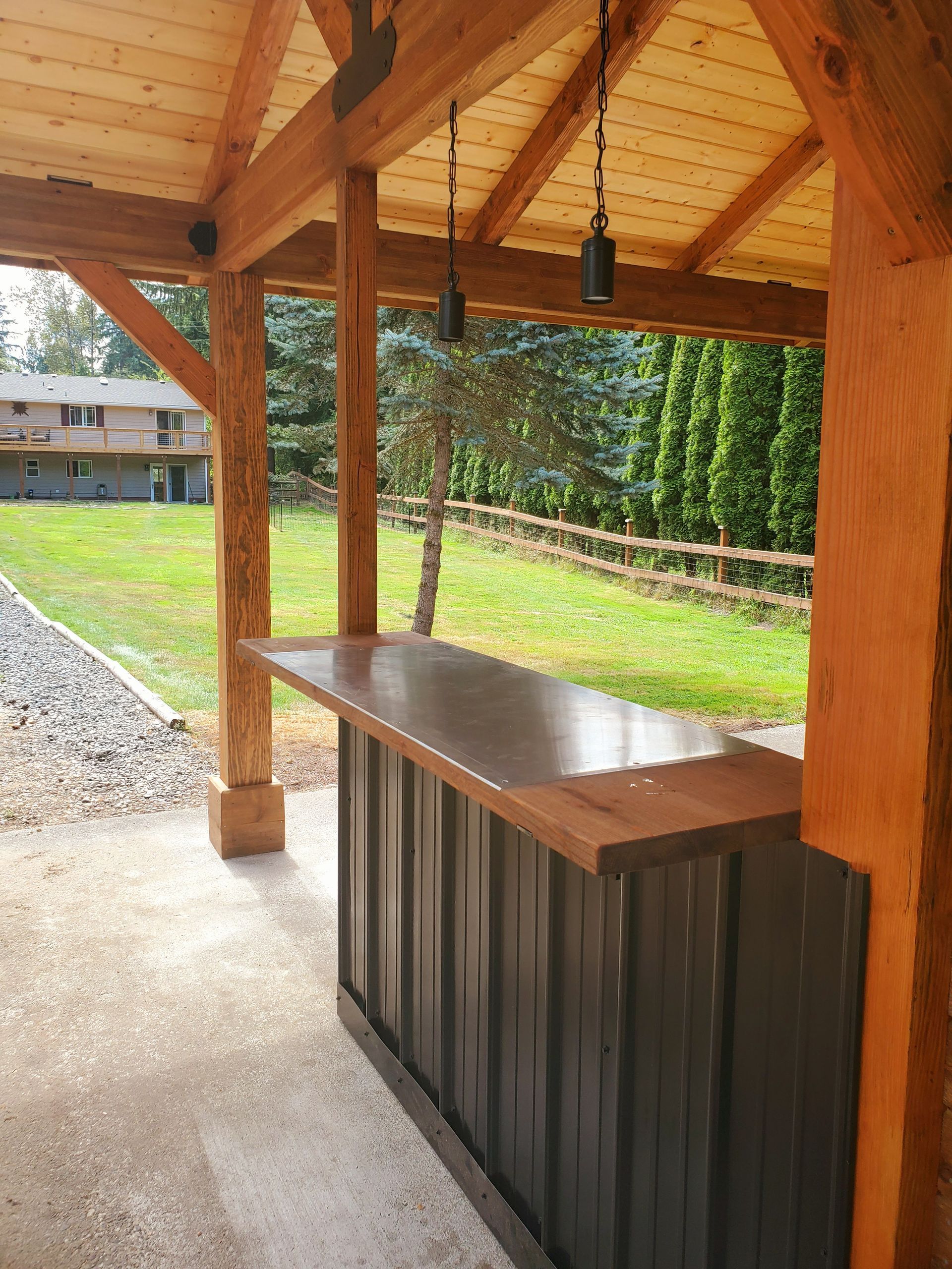 Outdoor bar with wooden frame, metal siding, concrete countertop, and pendant lights.