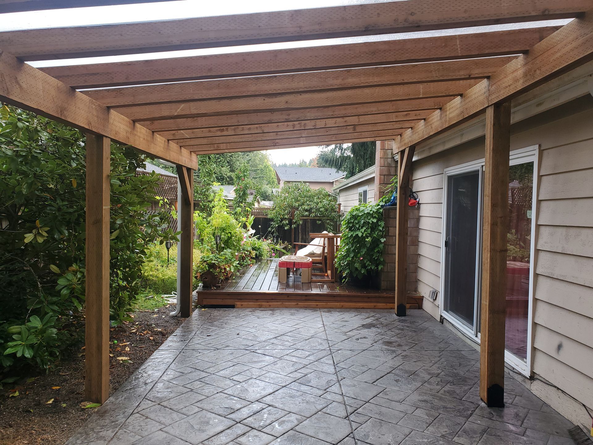 Wooden pergola over a concrete patio with a view of a backyard garden.